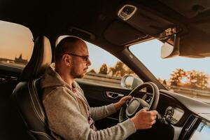 een Mens met een zonnebril het rijden een auto Bij zonsondergang. de concept van auto reizen foto