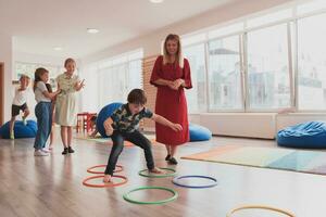 klein kinderkamer school- kinderen met vrouw leraar Aan verdieping binnenshuis in klas, aan het doen oefening. jumping over- hula hoepel cirkels bijhouden Aan de vloer. foto