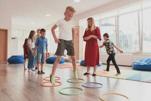 klein kinderkamer school- kinderen met vrouw leraar Aan verdieping binnenshuis in klas, aan het doen oefening. jumping over- hula hoepel cirkels bijhouden Aan de vloer. foto