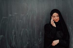 jong modern moslim bedrijf vrouw gebruik makend van smartphone vervelend hijab kleren in voorkant van zwart schoolbord foto