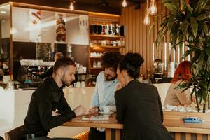 een groep van vrienden hangende uit in een cafe, en tussen hen is een tablet. foto