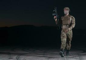 leger soldaat in gevecht uniformen met een aanval geweer, bord vervoerder en gevecht helm gaan Aan een gevaarlijk missie Aan een regenachtig nacht. foto