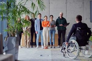 een groep van verschillend ondernemers verzamelen in een modern kantoor naar bespreken bedrijf ideeën en strategieën, terwijl een collega in een rolstoel doet mee hen. foto