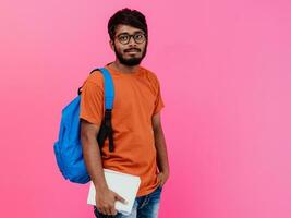 Indisch leerling met blauw rugzak, bril en notitieboekje poseren Aan roze achtergrond. de concept van onderwijs en scholing. tijd naar Gaan terug naar school- foto