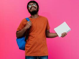 Indisch leerling met blauw rugzak, bril en notitieboekje poseren Aan roze achtergrond. de concept van onderwijs en scholing. tijd naar Gaan terug naar school- foto