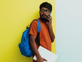 Indisch leerling met blauw rugzak, bril en notitieboekje gebruik makend van smarpthone en poseren Aan groen grijs achtergrond. de concept van onderwijs en scholing. tijd naar Gaan terug naar school- foto