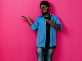 Indisch glimlachen jong leerling in blauw overhemd en bril poseren Aan roze achtergrond foto
