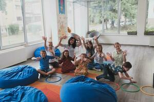 een gelukkig vrouw leraar zittend en spelen hand- spellen met een groep van weinig schoolkinderen foto