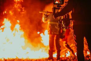 een cameraman met professioneel uitrusting en stabilisatie voor de camera opname de brandweerman terwijl het uitvoeren van werk in een brandend Woud foto