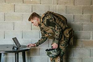 Amerikaans soldaat in leger uniform gebruik makend van laptop computer voor dar controlerend en naar blijven in contact met vrienden en familie foto