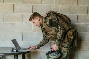 Amerikaans soldaat in leger uniform gebruik makend van laptop computer voor dar controlerend en naar blijven in contact met vrienden en familie foto