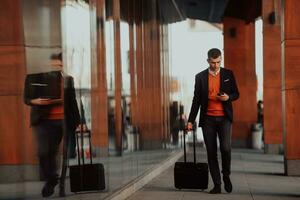 gaan naar luchthaven terminal. zelfverzekerd zakenman reiziger wandelen Aan stad straten en trekken zijn koffer drinken koffie en sprekend Aan smartphone foto