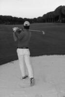 golfspeler raken een zand bunker schot Aan zonsondergang foto