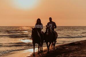 een liefhebbend paar in zomer kleren rijden een paard Aan een zanderig strand Bij zonsondergang. zee en zonsondergang in de achtergrond. selectief focus foto