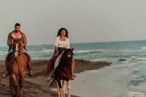 een liefhebbend paar in zomer kleren rijden een paard Aan een zanderig strand Bij zonsondergang. zee en zonsondergang in de achtergrond. selectief focus foto