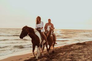 een liefhebbend paar in zomer kleren rijden een paard Aan een zanderig strand Bij zonsondergang. zee en zonsondergang in de achtergrond. selectief focus foto