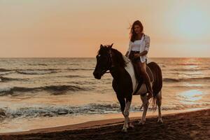 vrouw in zomer kleren geniet rijden een paard Aan een mooi zanderig strand Bij zonsondergang. selectief focus foto