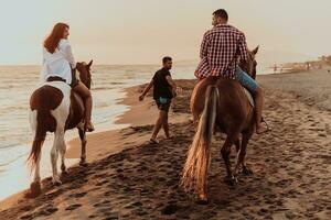 een liefhebbend paar in zomer kleren rijden een paard Aan een zanderig strand Bij zonsondergang. zee en zonsondergang in de achtergrond. selectief focus foto