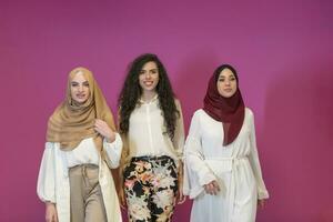 drie moslim Dames in hijab in een modern kleren houding tegen een roze achtergrond foto