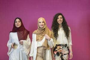 drie moslim Dames in hijab in een modern kleren houding tegen een roze achtergrond foto