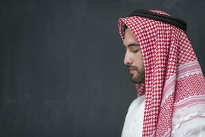 een jong Arabisch Mens in traditioneel kleren maken een traditioneel gebed naar god houdt zijn handen in bidden gebaar in voorkant van een zwart achtergrond foto