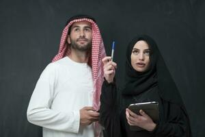 jong moslim bedrijf paar in modieus hijab jurk gebruik makend van smartphone en tablet in voorkant van zwart achtergrond foto
