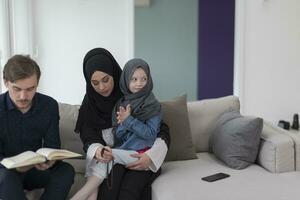 traditioneel moslim familie ouders met kinderen lezing koran en bidden samen Aan de sofa voordat iftar avondeten gedurende een Ramadan feest Bij huis foto