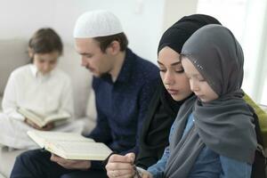 traditioneel moslim familie ouders met kinderen lezing koran en bidden samen Aan de sofa voordat iftar avondeten gedurende een Ramadan feest Bij huis foto