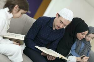 traditioneel moslim familie ouders met kinderen lezing koran en bidden samen Aan de sofa voordat iftar avondeten gedurende een Ramadan feest Bij huis foto