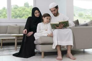 traditioneel moslim familie ouders met kinderen lezing koran en bidden samen Aan de sofa voordat iftar avondeten gedurende een Ramadan feest Bij huis foto