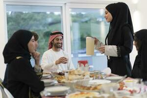 eid mubarak moslim familie hebben iftar avondeten drinken water naar breken feest. aan het eten traditioneel voedsel gedurende Ramadan feesten maand Bij huis. de Islamitisch halal aan het eten en drinken Bij modern western isla foto