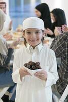 eid mubarak moslim familie hebben iftar avondeten weinig jongen Holding een bord vol van zoet datums naar breken feest. aan het eten traditioneel voedsel gedurende Ramadan feesten maand Bij huis. de Islamitisch halal aan het eten foto