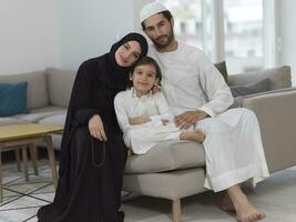 traditioneel moslim familie ouders met kinderen lezing koran en bidden samen Aan de sofa voordat iftar avondeten gedurende een Ramadan feest Bij huis foto