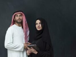 jong moslim bedrijf paar in modieus hijab jurk gebruik makend van smartphone en tablet in voorkant van zwart achtergrond foto