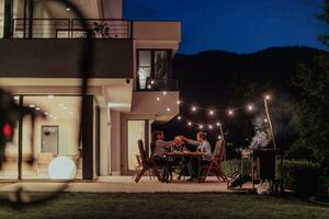 een groep van jong verschillend mensen hebben avondeten Aan de terras van een modern huis in de avond. pret voor vrienden en familie. viering van vakantie, bruiloften met barbecue. foto