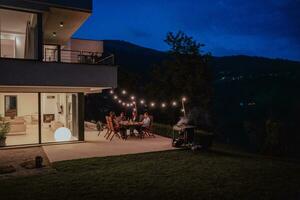 een groep van jong verschillend mensen hebben avondeten Aan de terras van een modern huis in de avond. pret voor vrienden en familie. viering van vakantie, bruiloften met barbecue. foto