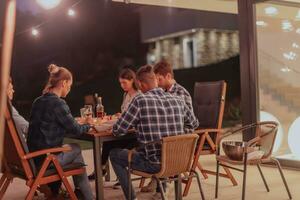 een groep van jong verschillend mensen hebben avondeten Aan de terras van een modern huis in de avond. pret voor vrienden en familie. viering van vakantie, bruiloften met barbecue. foto