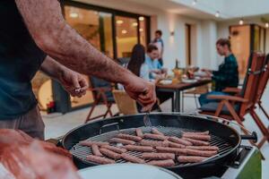 een groep van vrienden en familie barbecue samen in de avond Aan de terras in voorkant van een groot modern huis foto