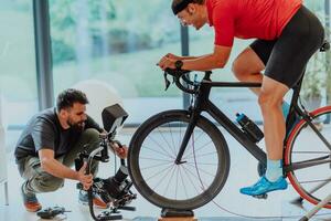 een cameraman filmen een atleet rijden een triatlon fiets Aan een simulatie machine in een modern leven kamer. opleiding in pandemisch conditie. foto