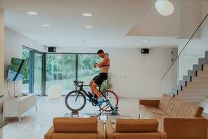 een Mens rijden een triatlon fiets Aan een machine simulatie in een modern leven kamer. opleiding gedurende pandemisch conditie. foto