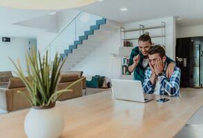 een jong getrouwd paar is pratend naar ouders, familie en vrienden Aan een video telefoontje via een laptop terwijl zittend in de leven kamer van hun modern huis foto