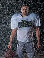 Amerikaans Amerikaans voetbal veld- eenzaam atleet krijger staand Aan een veld- houdt zijn helm en klaar naar Speel. speler voorbereidingen treffen naar rennen, aanval en partituur touchdown. regenachtig nacht met dramatisch mist, blauw licht foto
