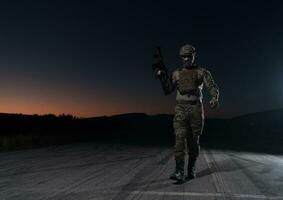 leger soldaat in gevecht uniformen met een aanval geweer, bord vervoerder en gevecht helm gaan Aan een gevaarlijk missie Aan een regenachtig nacht. foto