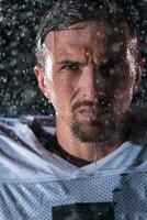 Amerikaans Amerikaans voetbal veld- eenzaam atleet krijger staand Aan een veld- houdt zijn helm en klaar naar Speel. speler voorbereidingen treffen naar rennen, aanval en partituur touchdown. regenachtig nacht met dramatisch mist, blauw licht foto