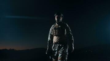 leger soldaat in gevecht uniformen met een aanval geweer, bord vervoerder en gevecht helm gaan Aan een gevaarlijk missie Aan een regenachtig nacht. foto