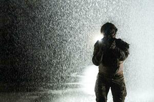 leger soldaat in gevecht uniformen met een aanval geweer, bord vervoerder en gevecht helm gaan Aan een gevaarlijk missie Aan een regenachtig nacht. foto