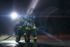 brandweerlieden gebruik makend van een water slang naar elimineren een brand gevaar. team van vrouw en mannetje brandweer in gevaarlijk redden missie. foto