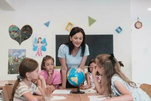 vrouw leraar met kinderen in aardrijkskunde klasse op zoek Bij wereldbol. kant visie van groep van verschillend gelukkig school- kinderen met wereldbol in klas Bij school. foto