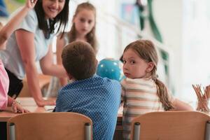 vrouw leraar met kinderen in aardrijkskunde klasse op zoek Bij wereldbol. kant visie van groep van verschillend gelukkig school- kinderen met wereldbol in klas Bij school. foto