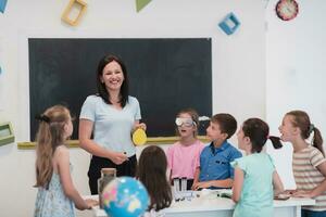 elementair school- wetenschap klas enthousiast leraar legt uit chemie naar verschillend groep van kinderen, weinig jongen mengsels Chemicaliën in bekers. kinderen leren met interesseren foto